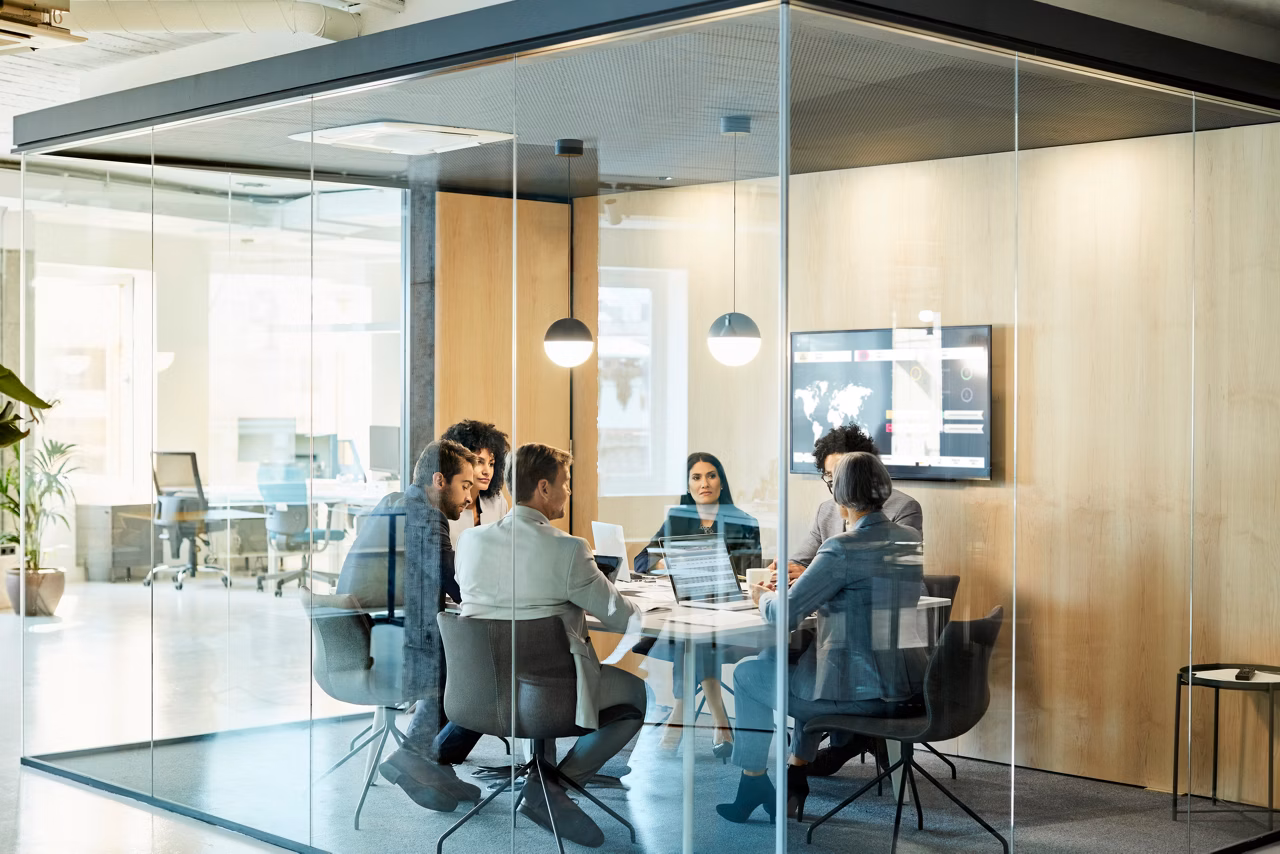 Business colleagues sitting at conference table seen through glass wall. Multi-ethnic coworkers are discussing in board room at office. They are planning strategy.