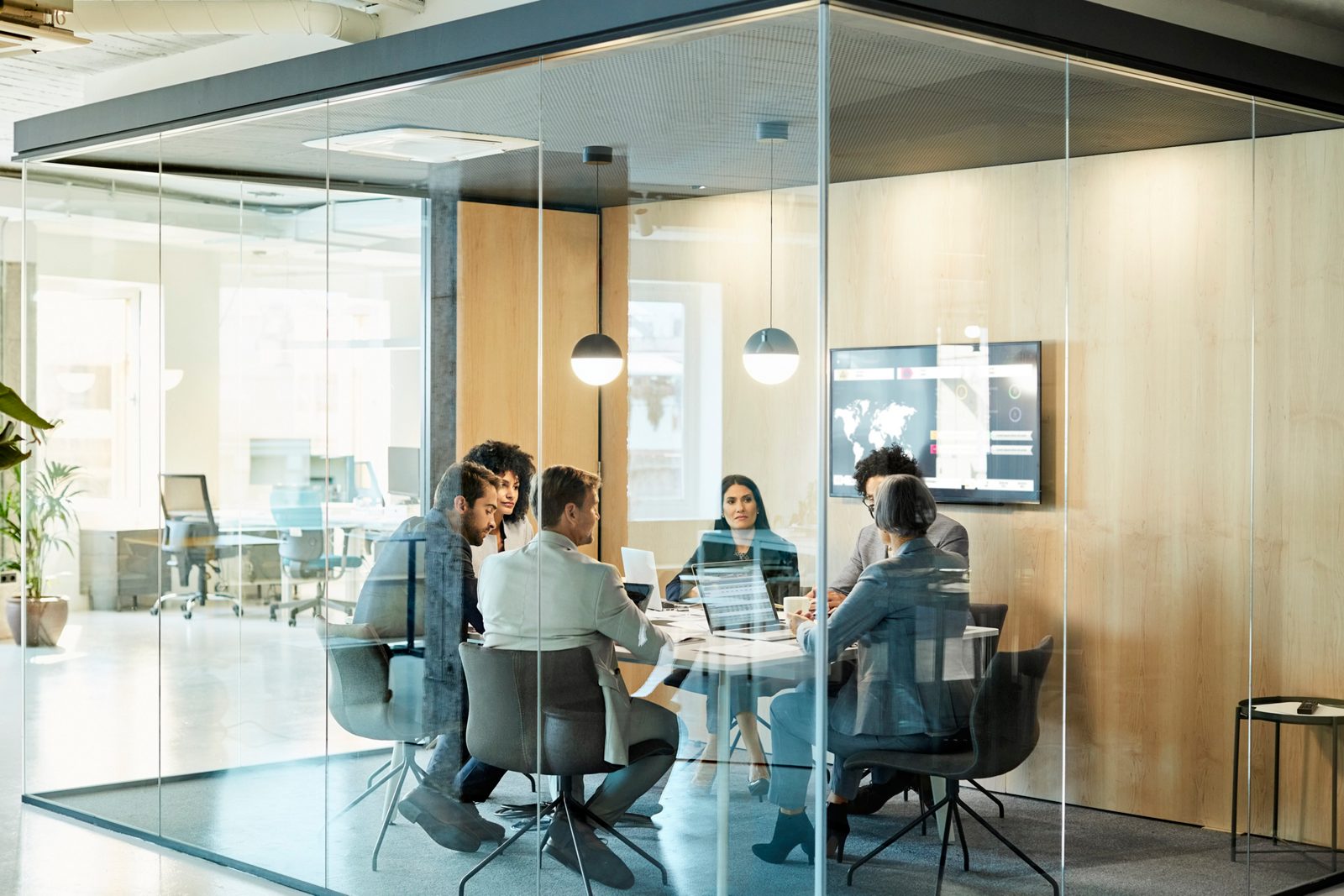 Business colleagues sitting at conference table seen through glass wall. Multi-ethnic coworkers are discussing in board room at office. They are planning strategy.