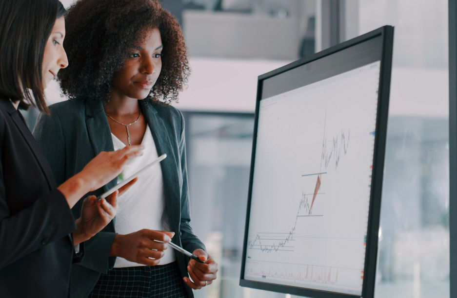 Shot of two young businesswomen using an interactive whiteboard to analyse data in a modern office