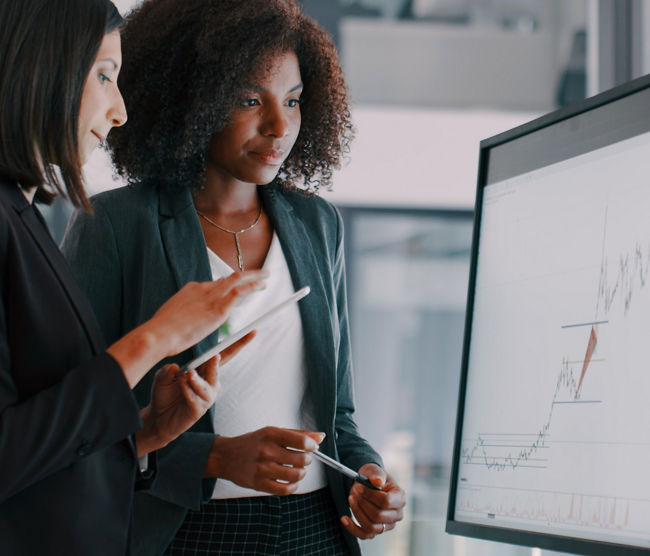 Shot of two young businesswomen using an interactive whiteboard to analyse data in a modern office