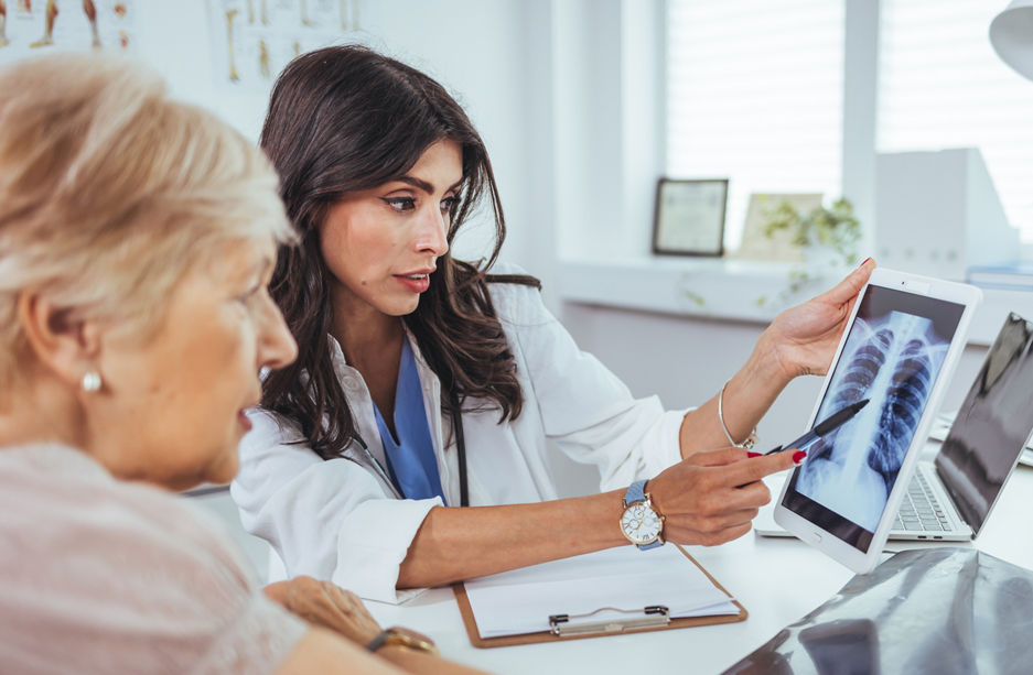 Doctor shows results to old patient x-ray of the lungs, smoking cigarettes problem. Doctor explaining lungs x-ray on Tablet PC screen to young patient. Doctor showing female patient x-ray shot in clinic office. Coronavirus chest X-ray.