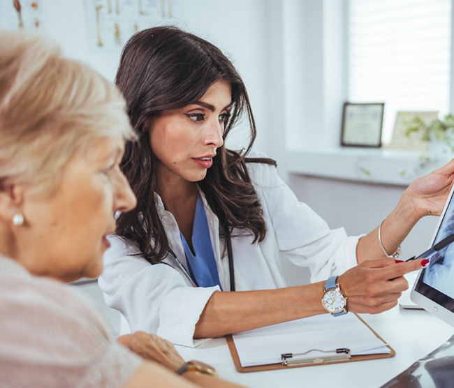 Doctor shows results to old patient x-ray of the lungs, smoking cigarettes problem. Doctor explaining lungs x-ray on Tablet PC screen to young patient. Doctor showing female patient x-ray shot in clinic office. Coronavirus chest X-ray.