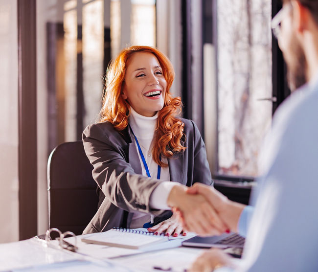  a young woman smiling and shaking hands with a client, after concluding a contract