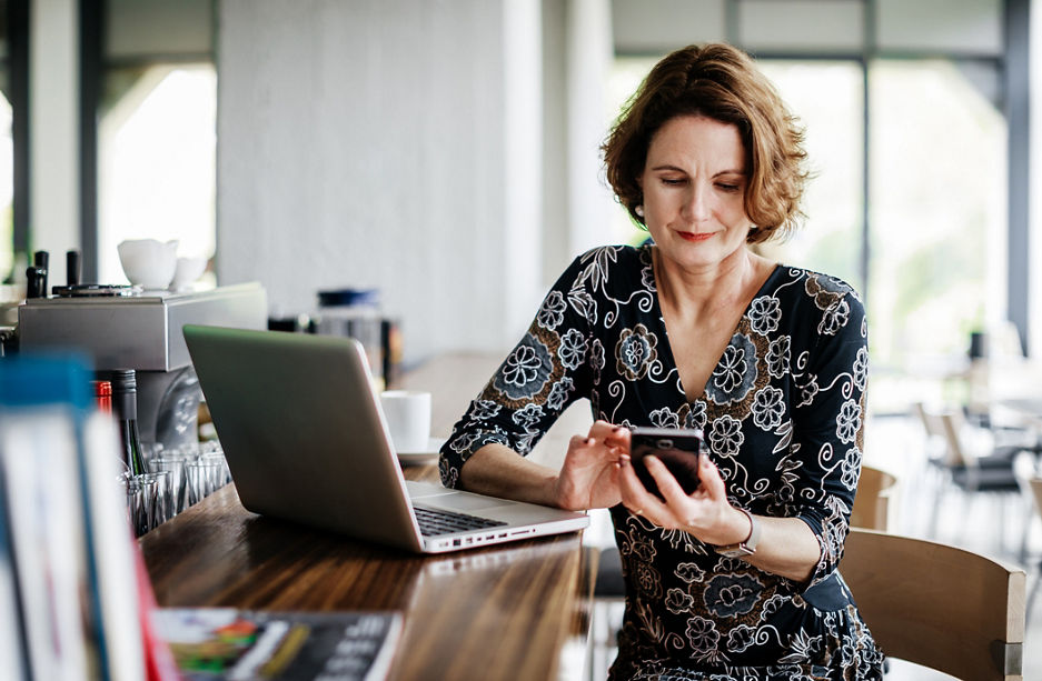 A businesswoman sitting at a restaurant bar using her smartphone after lunch.