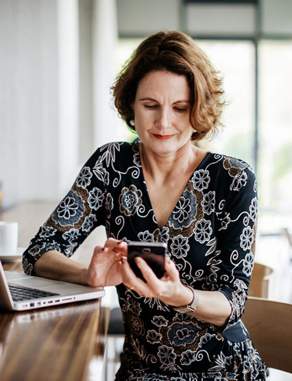 A businesswoman sitting at a restaurant bar using her smartphone after lunch.