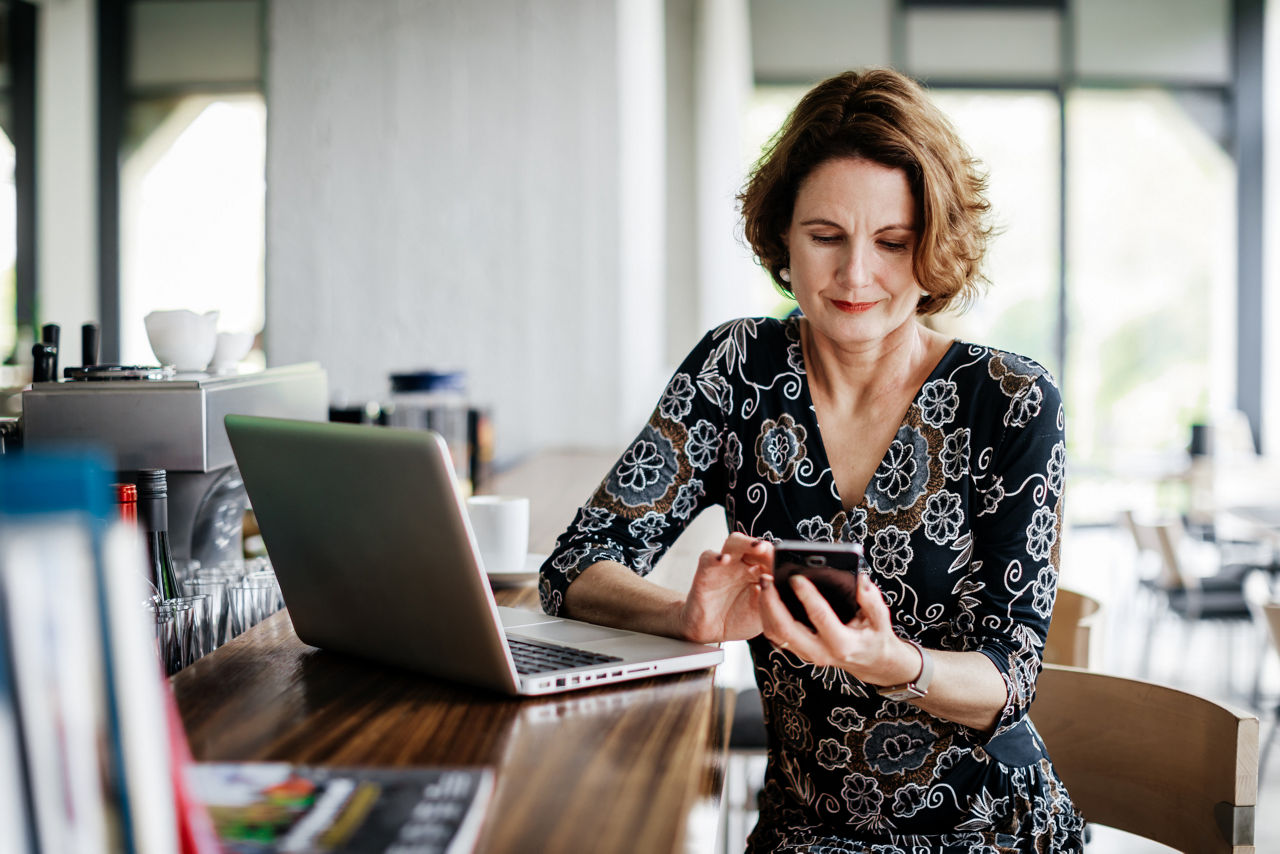 A businesswoman sitting at a restaurant bar using her smartphone after lunch.