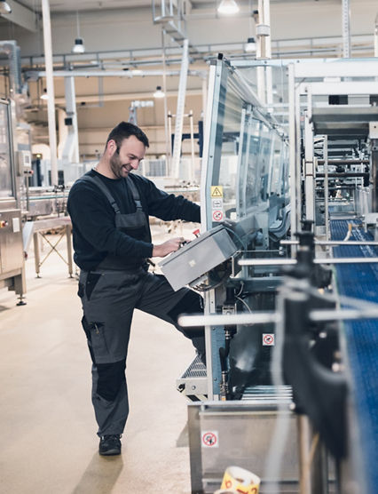 Happy smiled worker doing his job on Robotic factory line for processing and quality control of pure spring water bottled into canisters. Low light and small amount of noise visible.