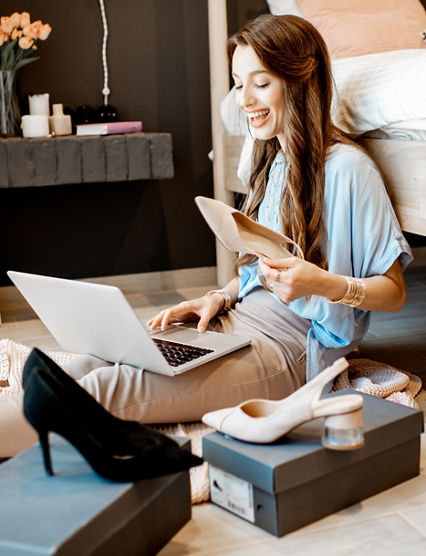 Young woman unpacking parcels with footwear, feeling happy with new online purchases, sitting in the bedroom at home