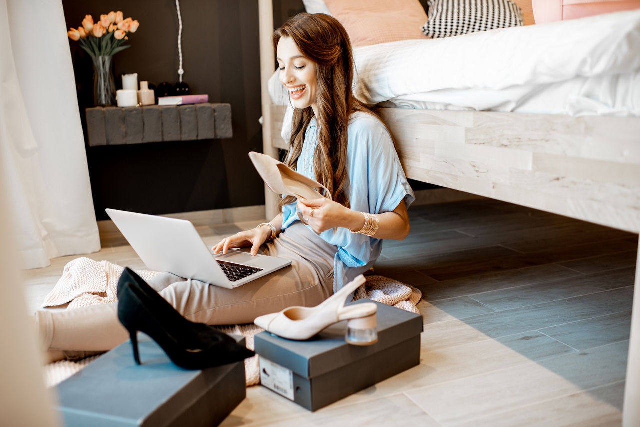 Young woman unpacking parcels with footwear, feeling happy with new online purchases, sitting in the bedroom at home