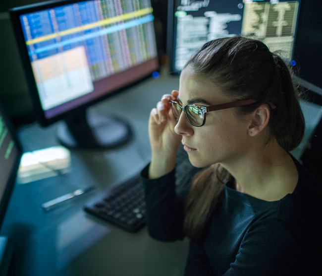Woman analyzing code on multiple computer monitors