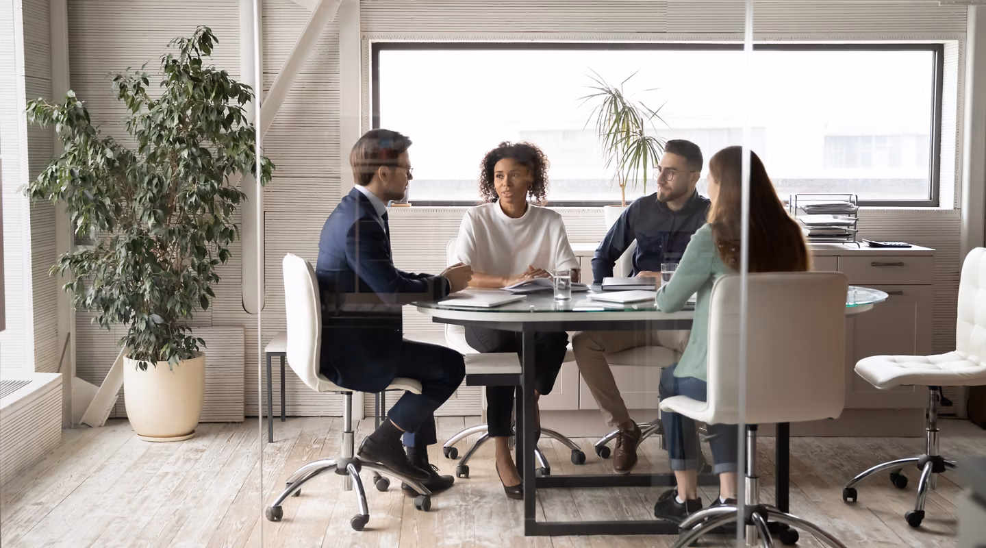 Diverse international businesspeople sit at desk in office boardroom talk discuss ideas together. Multiracial colleagues brainstorm at team group business meeting or briefing. Cooperation concept.