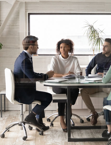 Diverse international businesspeople sit at desk in office boardroom talk discuss ideas together. Multiracial colleagues brainstorm at team group business meeting or briefing. Cooperation concept.