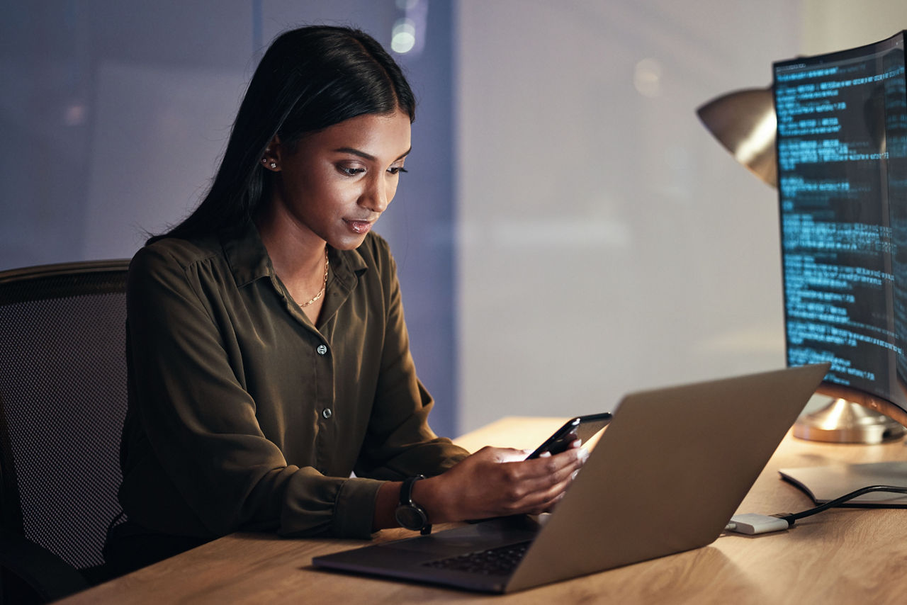 Laptop, phone and business woman on coding, software development and programming script for cybersecurity. Night, mobile research and multimedia programmer or IT person on computer with data analysis.