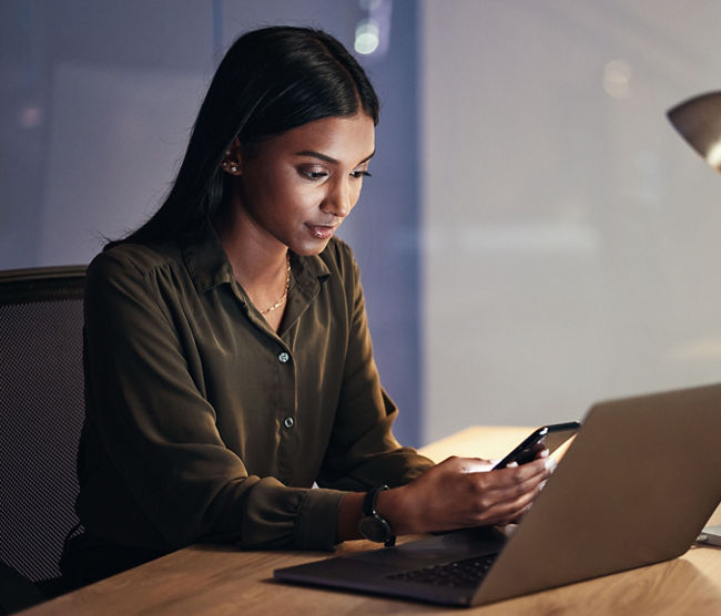 Laptop, phone and business woman on coding, software development and programming script for cybersecurity. Night, mobile research and multimedia programmer or IT person on computer with data analysis.