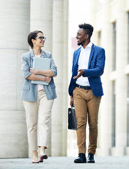 Happy excited office colleagues in stylish outfits talking about work when walking over street in summer