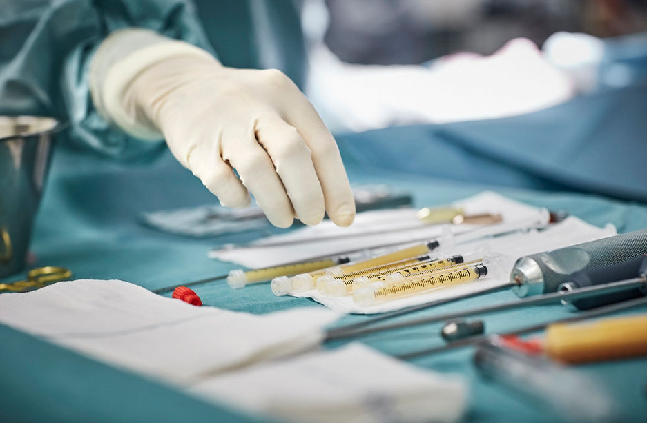Cropped image of female surgeon reaching for syringes on table. Close-up of healthcare worker's hand wearing surgical glove. She is in emergency room.
