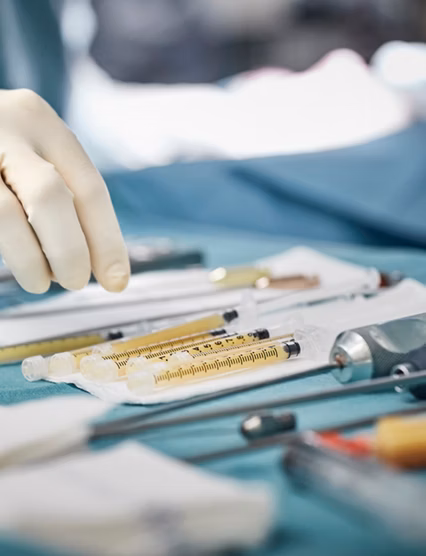 Cropped image of female surgeon reaching for syringes on table. Close-up of healthcare worker's hand wearing surgical glove. She is in emergency room.