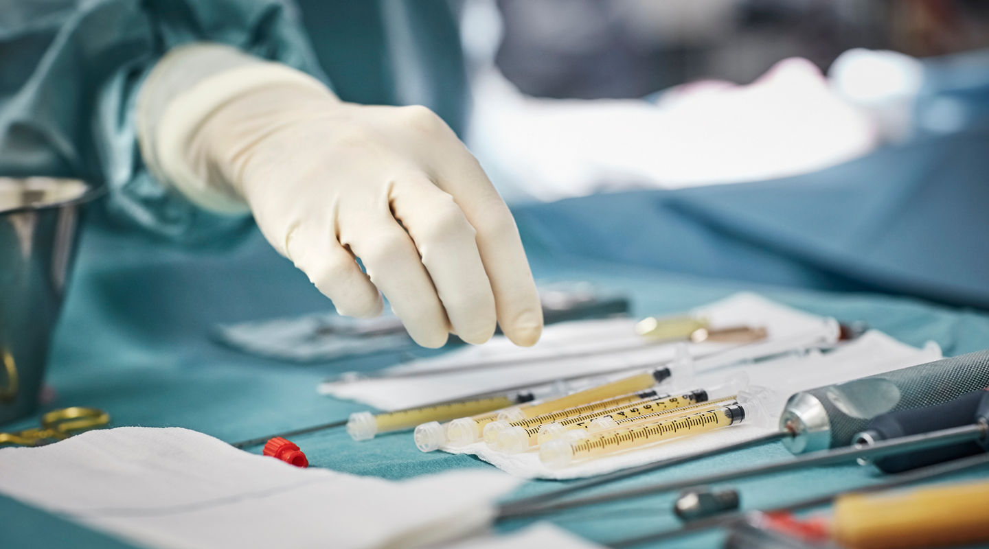 Cropped image of female surgeon reaching for syringes on table. Close-up of healthcare worker's hand wearing surgical glove. She is in emergency room.