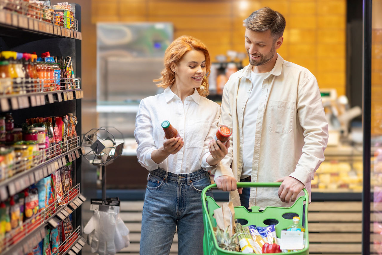 Happy European family shopping groceries in supermarket, choose what to buy, walking with trolley, standing near shelves in store aisle