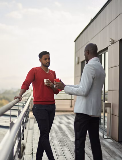 Businessmen in 30s and 40s standing face to face on modern office outdoor terrace enjoying relaxed exchange of ideas.