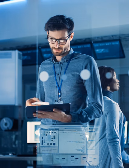 In Technology Research Facility: Chief Engineer Stands in the Middle of the Lab and Uses Tablet Computer. Team of Industrial Engineers, Developers Work on Engine Design Use Digital Whiteboard and Computers