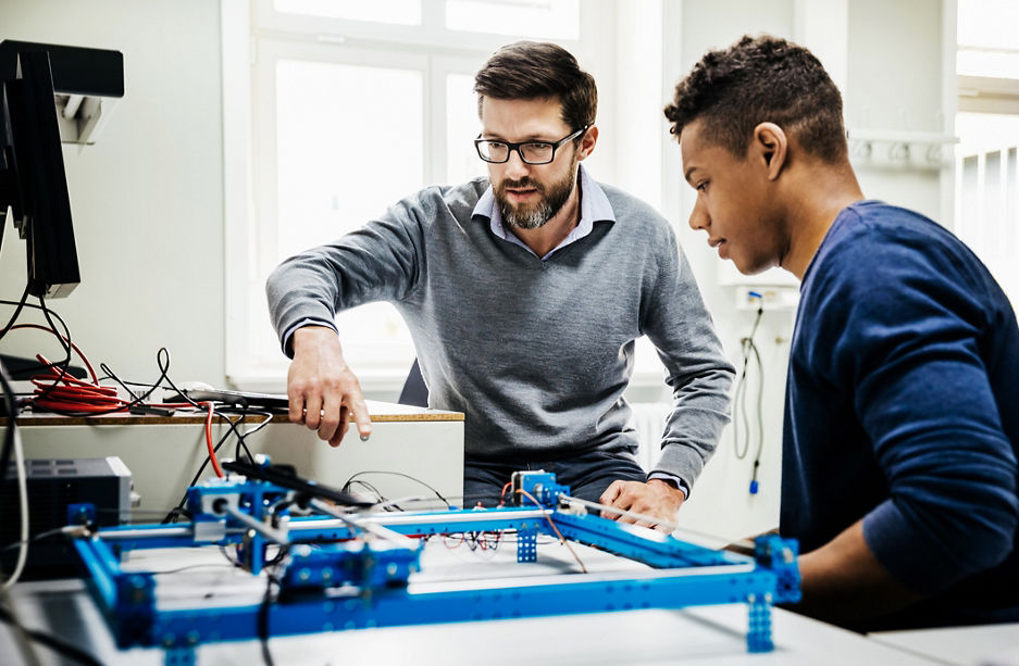 An engineering tutor assisting one of his students with a technical problem during teaching session at university.