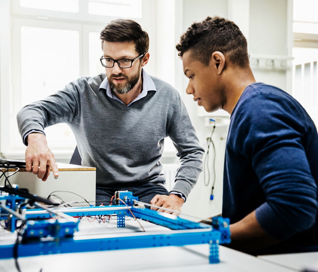 An engineering tutor assisting one of his students with a technical problem during teaching session at university.