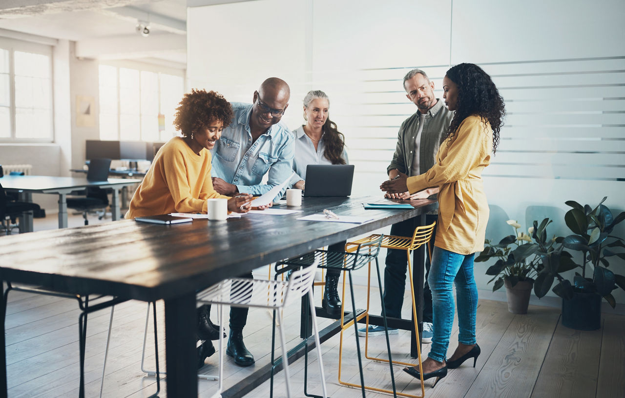 Smiling group of diverse businesspeople talking while working together around a table in a bright modern office