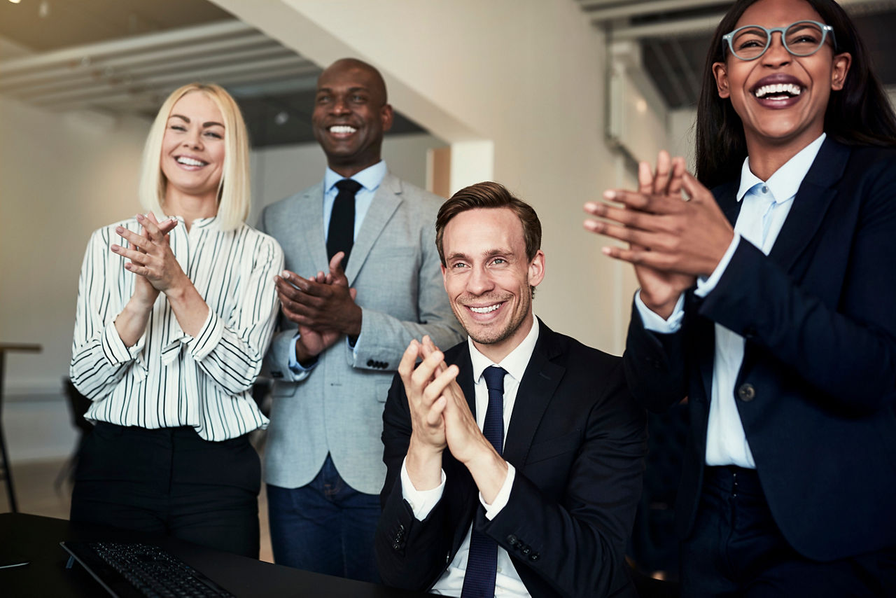 Smiling group of diverse businesspeople clapping while watching a presentation together in an office