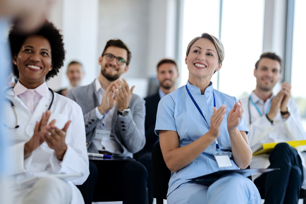 Group of happy healthcare workers and business people applauding after successful seminar in convention center. 