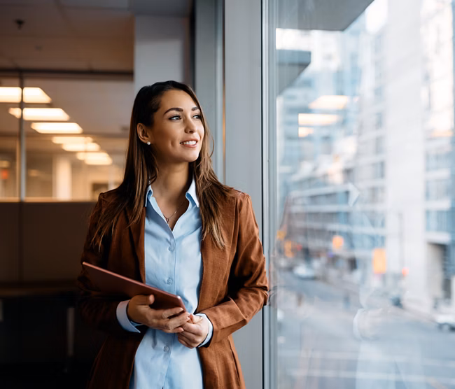 Pensive businesswoman with touchpad looking through window while working in office.