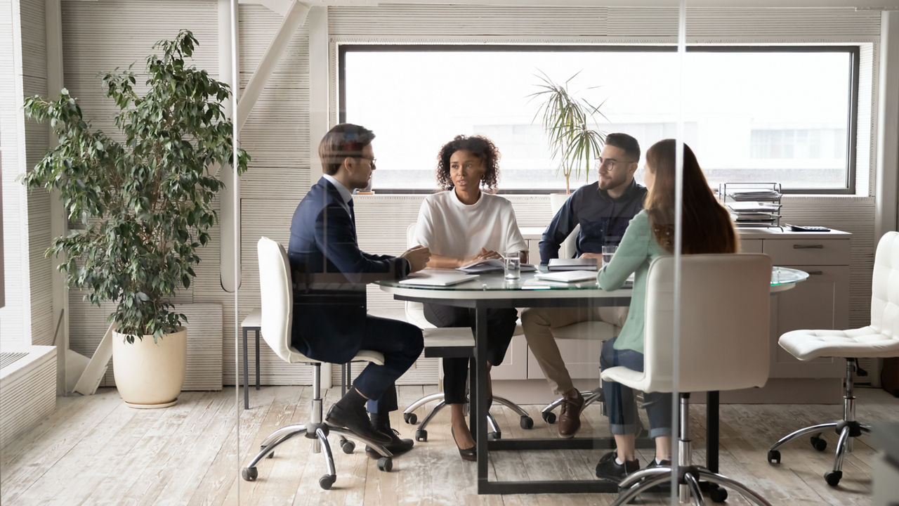 Diverse international businesspeople sit at desk in office boardroom talk discuss ideas together. Multiracial colleagues brainstorm at team group business meeting or briefing. Cooperation concept.