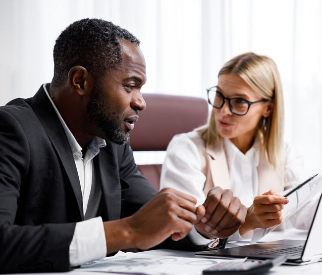 Two people analyze documents on a laptop while sitting at a table in the office. Business partners at work in the office are discussing projects. Multi-racial collaboration