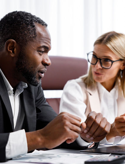 Two people analyze documents on a laptop while sitting at a table in the office. Business partners at work in the office are discussing projects. Multi-racial collaboration