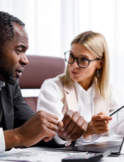 Two people analyze documents on a laptop while sitting at a table in the office. Business partners at work in the office are discussing projects. Multi-racial collaboration