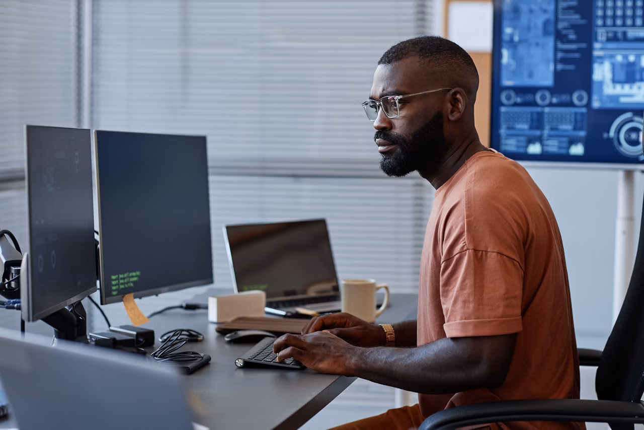 Side view of black software engineer using computer in high technology office, data systems and programming