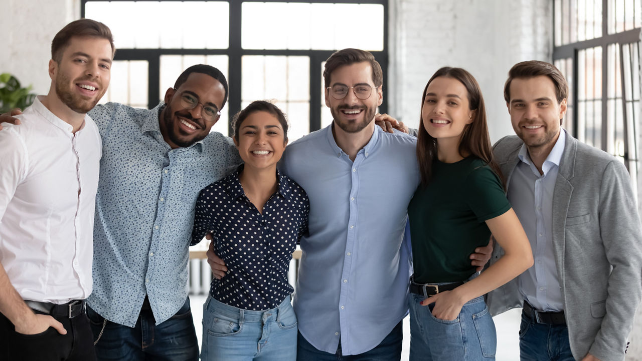 Group portrait of smiling diverse multiracial businesspeople look at camera posing in office together, happy multiethnic young colleagues hug show unity and support, teamwork, leadership concept