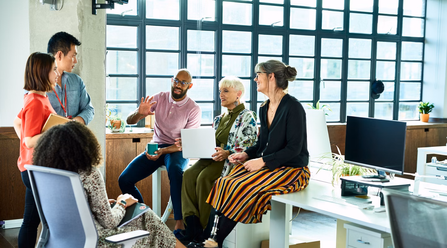 Diver group of mixed age and multi ethnic colleagues in discussion, mid adult man explaining and gesturing, woman with artificial limb smiling and listening