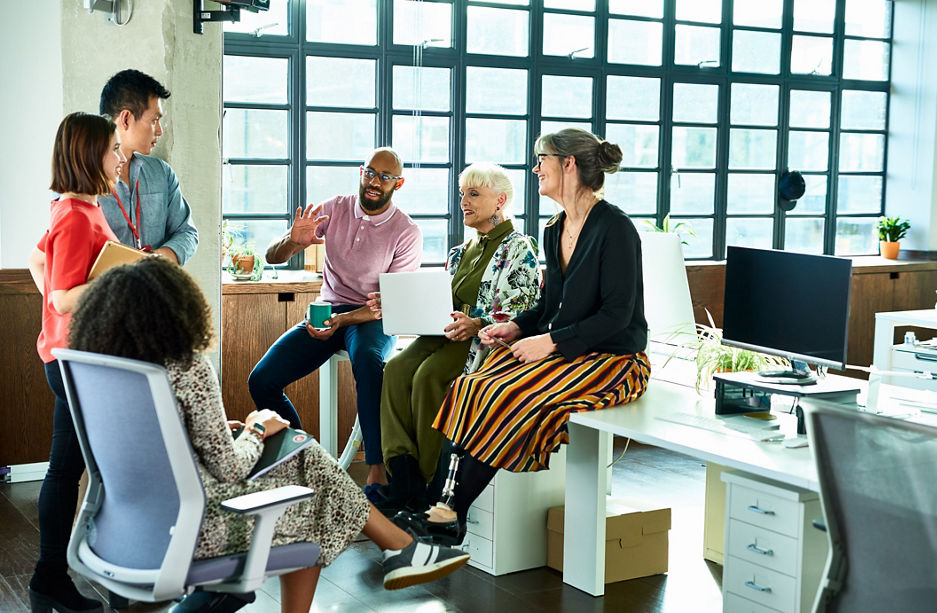 Diver group of mixed age and multi ethnic colleagues in discussion, mid adult man explaining and gesturing, woman with artificial limb smiling and listening