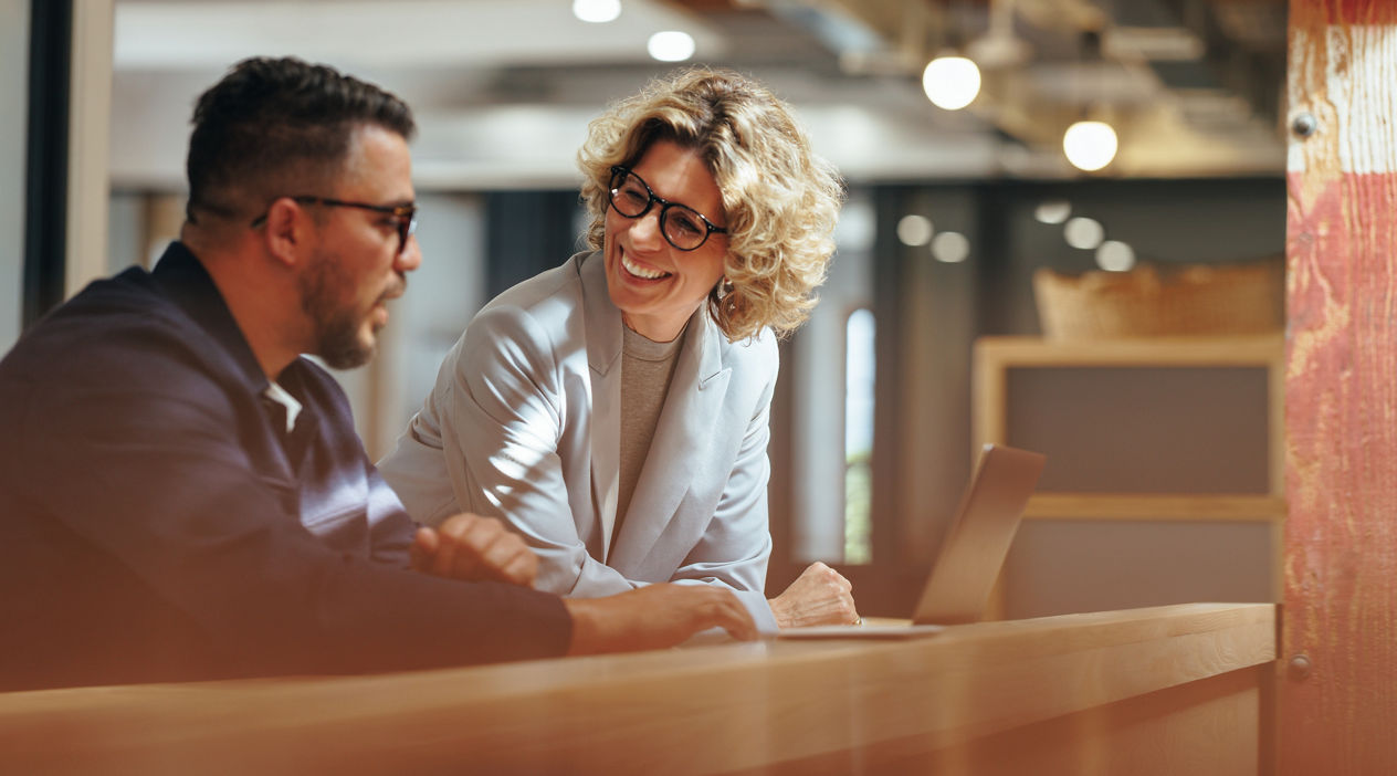 Successful business people working together in a coworking office. Two business professionals working on a tech project. Business colleagues talking to each other.