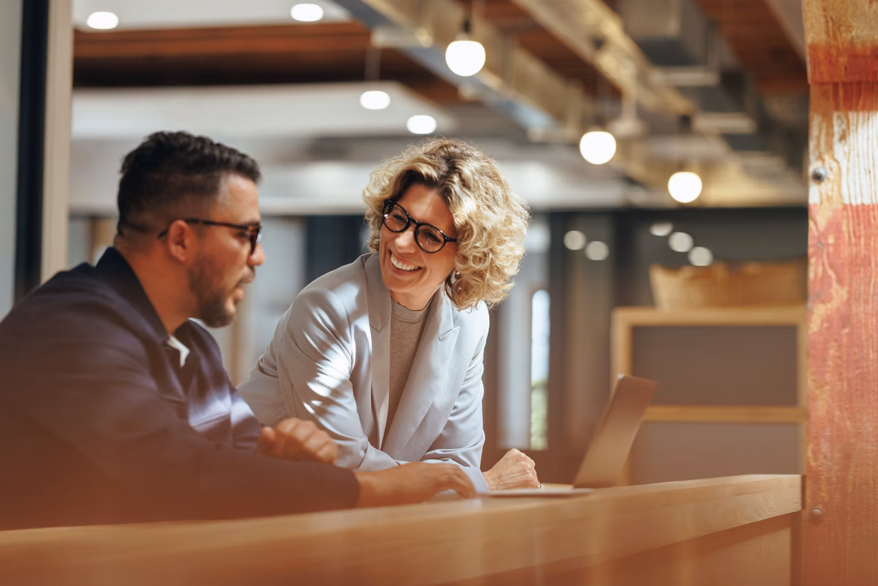Successful business people working together in a coworking office. Two business professionals working on a tech project. Business colleagues talking to each other.
