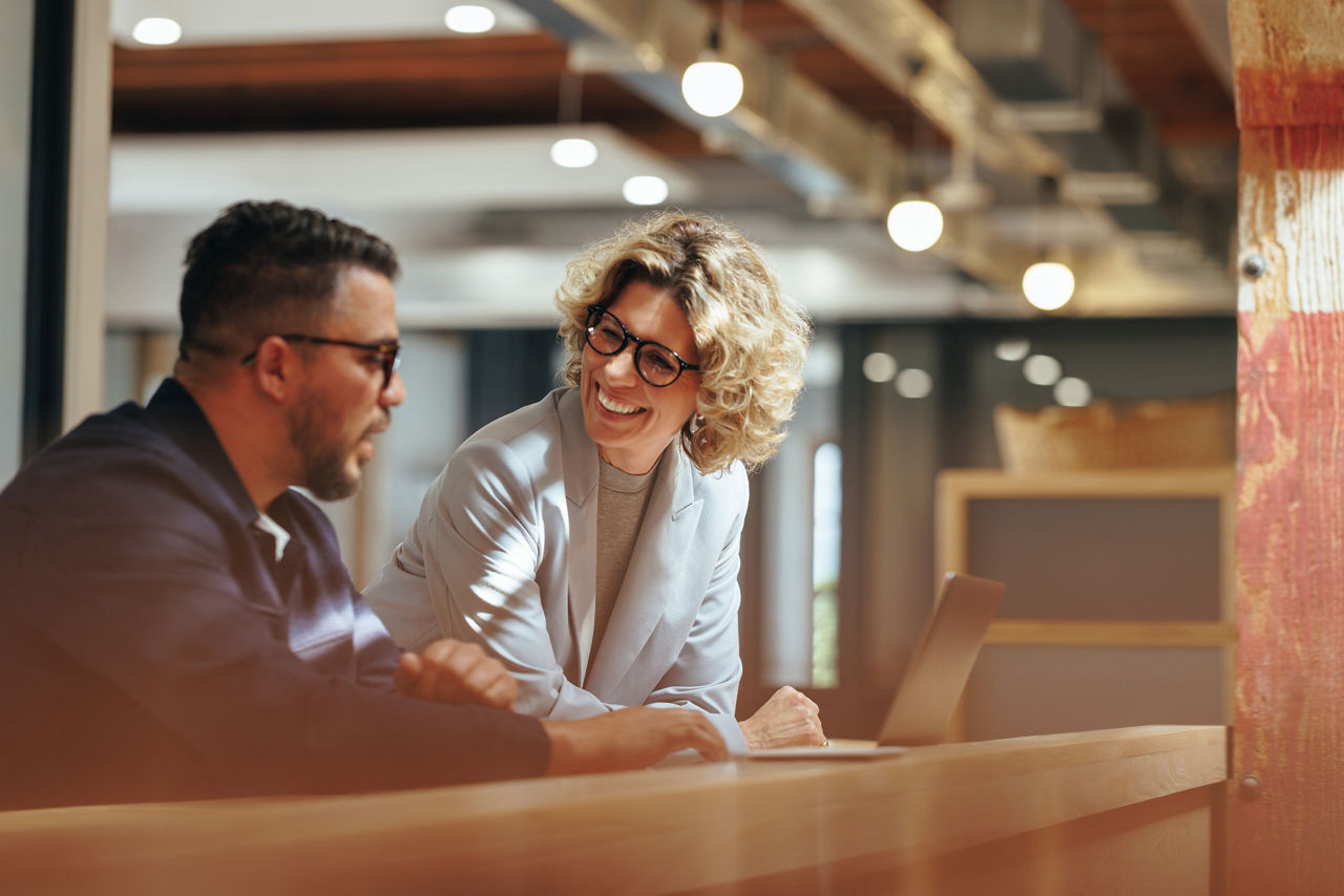 Successful business people working together in a coworking office. Two business professionals working on a tech project. Business colleagues talking to each other.