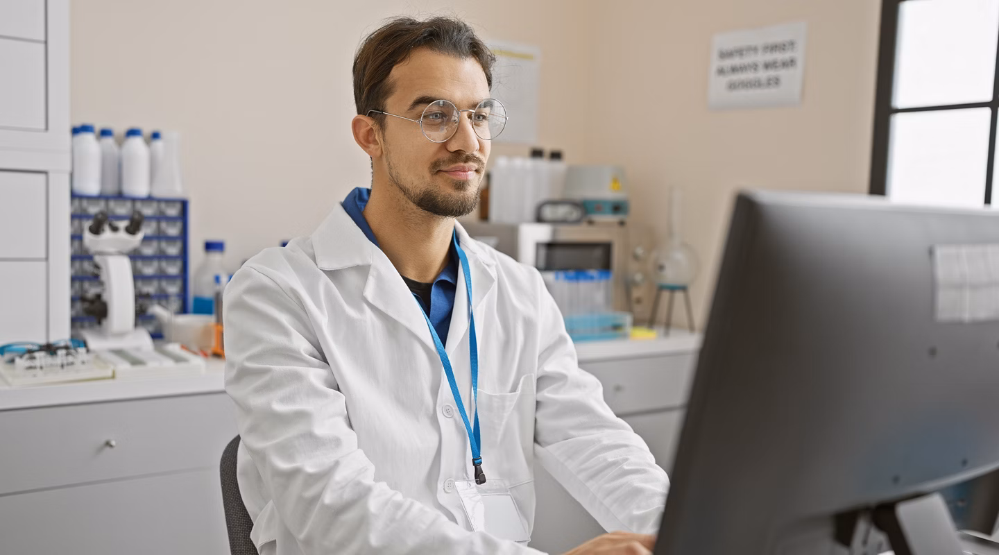 Hispanic scientist with beard working at computer in laboratory setting