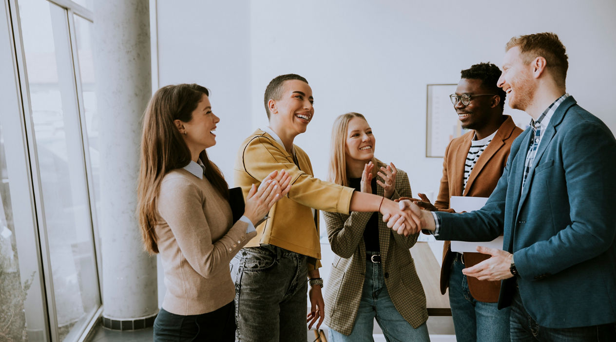 Memembers of young creative team shaking hands while working in the modern office