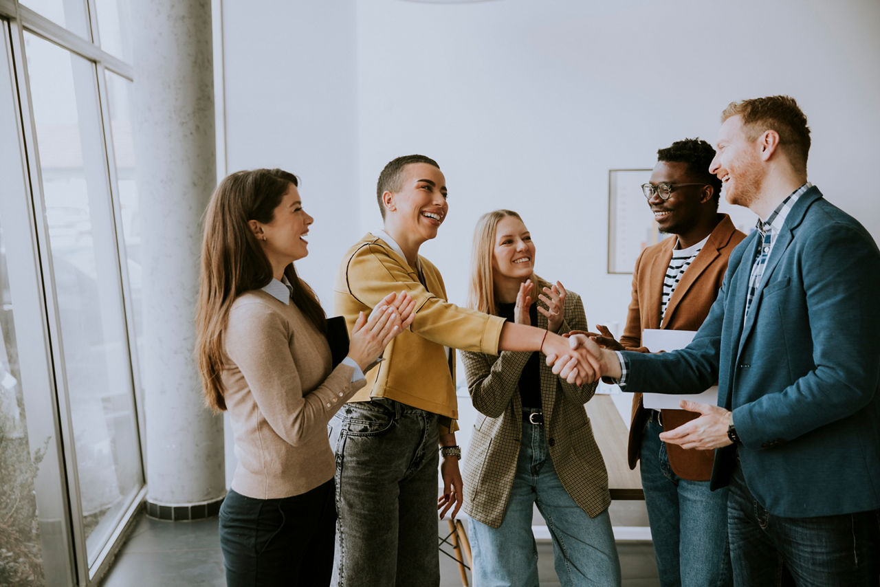 Memembers of young creative team shaking hands while working in the modern office
