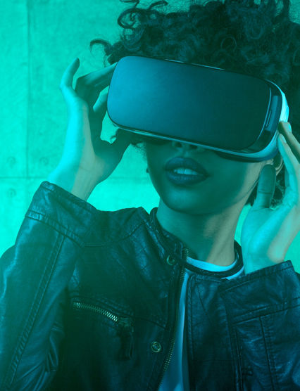 Young trendy woman using VR goggles standing in blue light looking away 