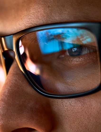 Close up view of focused businessman wears computer glasses for reducing eye strain blurred vision looking at pc screen with computer reflection using internet, reading, watching, working online late.