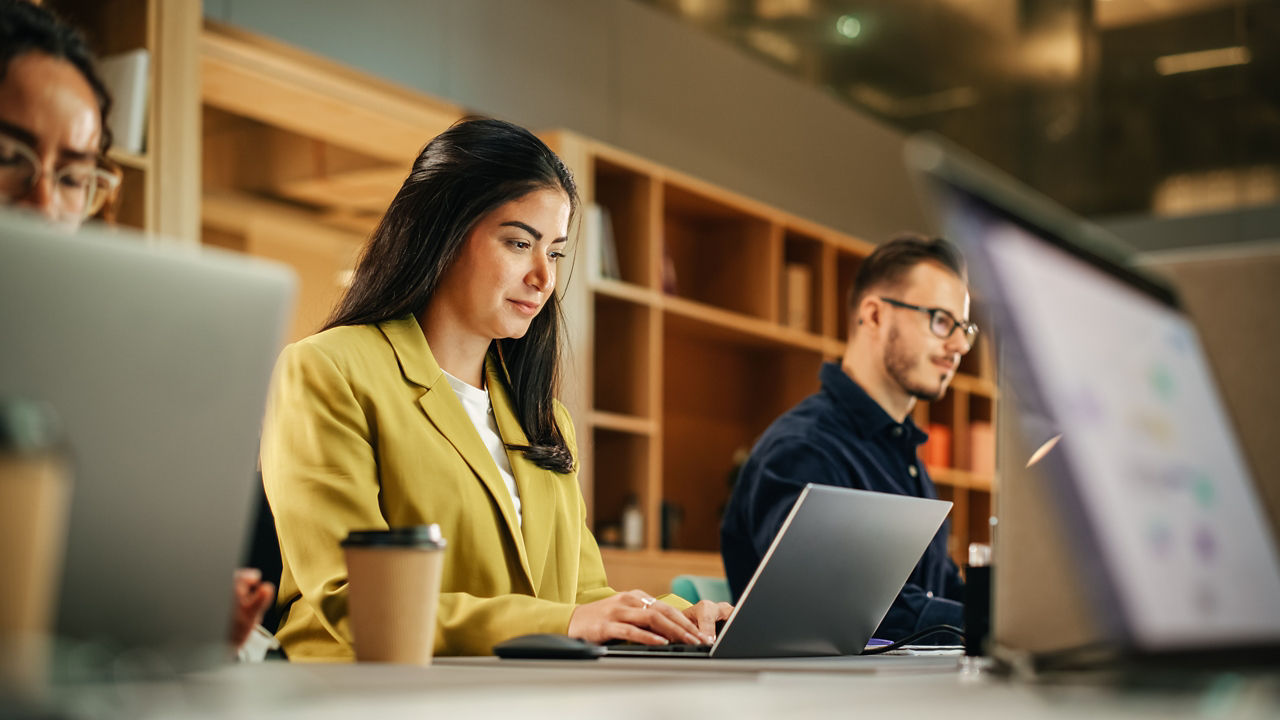 Group of Diverse Creative Team Members Using Laptops in an active Contemporary Office. Young Female Media Relations Manager Working on Brand Innovation Strategy and Collaborating with Colleagues.