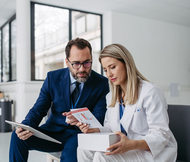 Portrait of pharmaceutical sales representative talking with doctor in medical building. Ambitious male sales representative in suit presenting new medication on tablet.