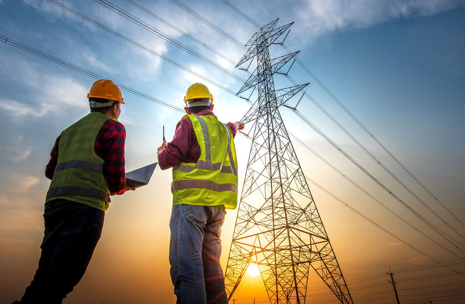 Picture of two electrical engineers using a notebook computer standing at a power station to view the planning work by producing electrical energy at high voltage electrodes.